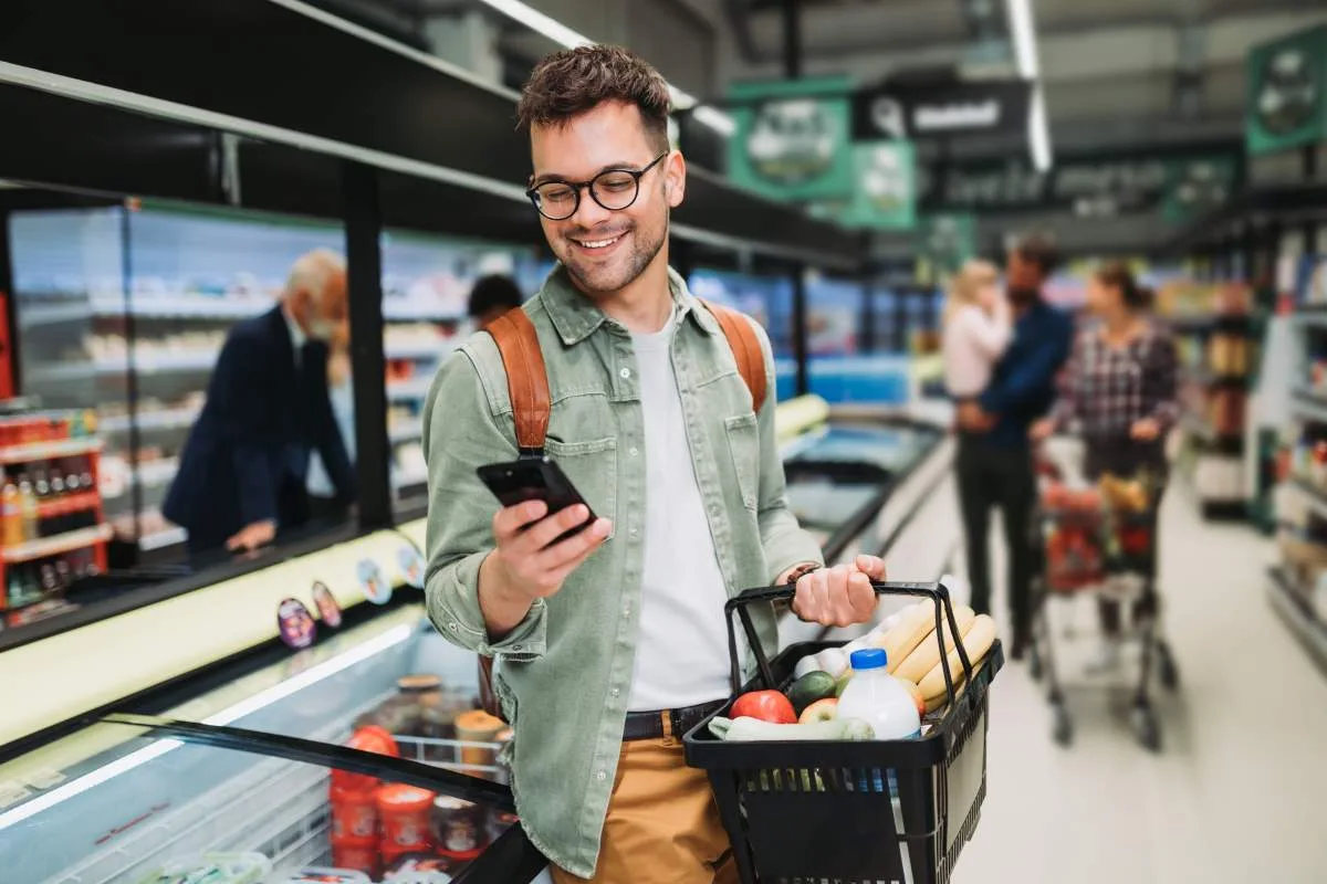 man on phone while grocery shopping with basket in hand